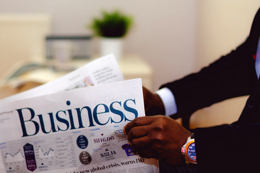 Person wearing a suit reading a newspaper with the headline "Business"